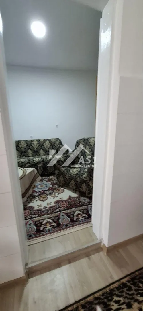 Pogled iz hodnika na dnevnu sobu sa garniturom i tepihom.