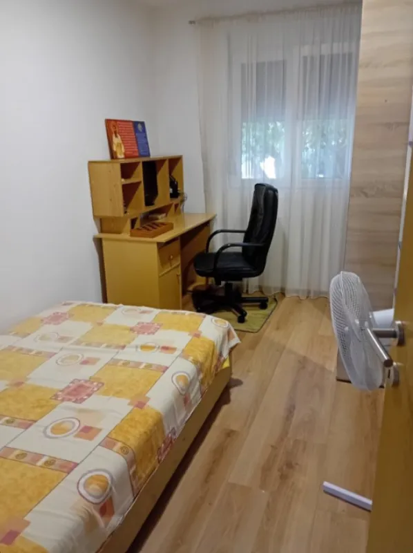Manja spavaća soba sa krevetom, radnim stolom i prozorom.