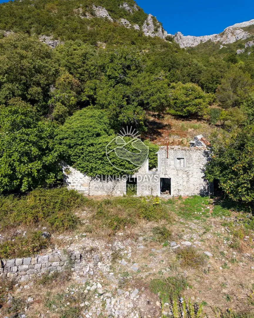 Ruševna kamena kuća zarasla u rastinje pod stijenom.
