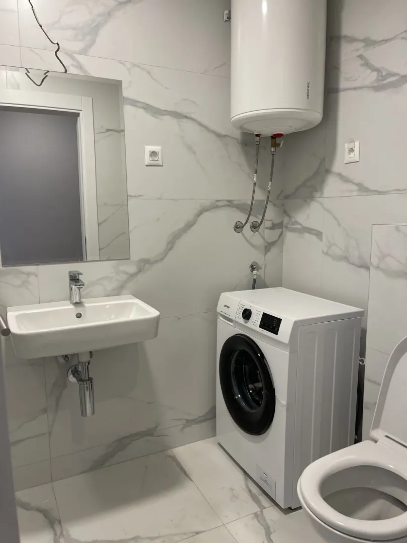 Svijetlo kupatilo sa veš mašinom, umivaonikom i bojlerom.