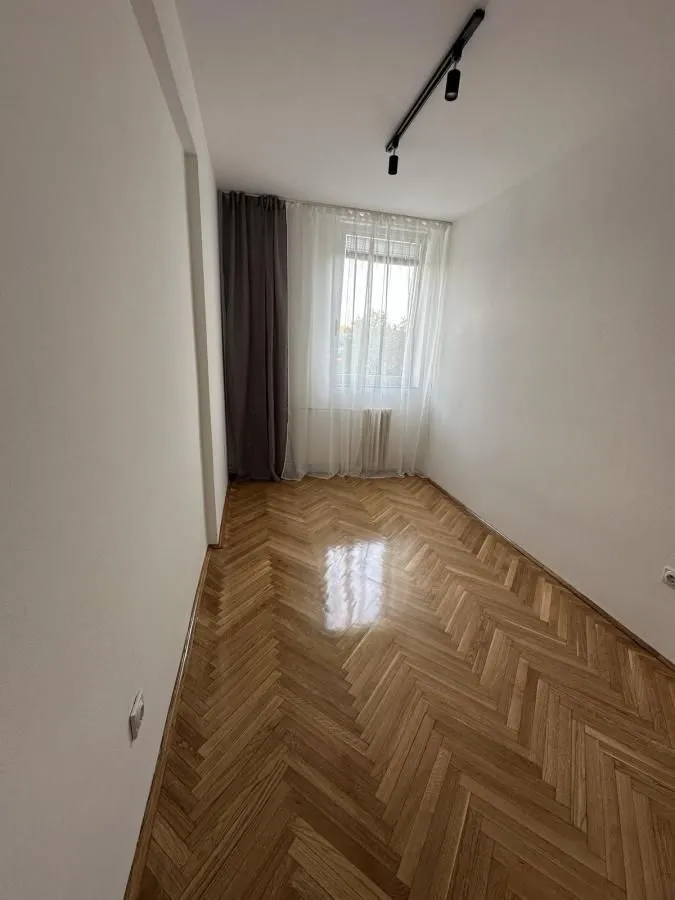 Prazna soba sa parketom i prozorom sa zavesama.