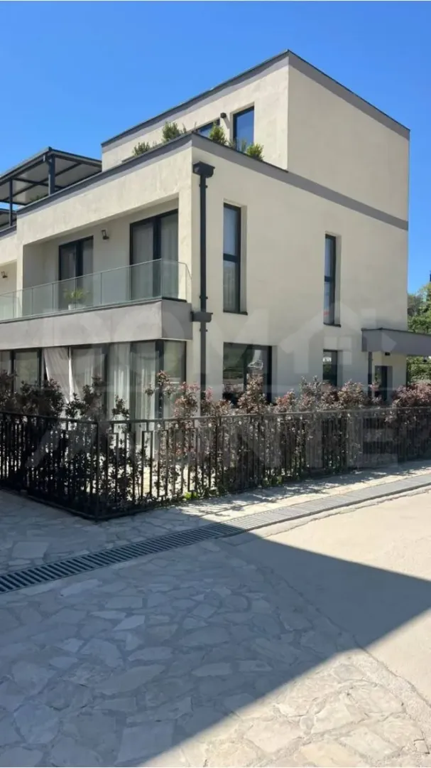 Exterior of a modern multi-family house with terraces and a yard.