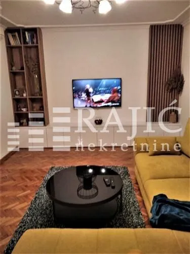 Living room with a sofa, coffee table and TV on the wall.