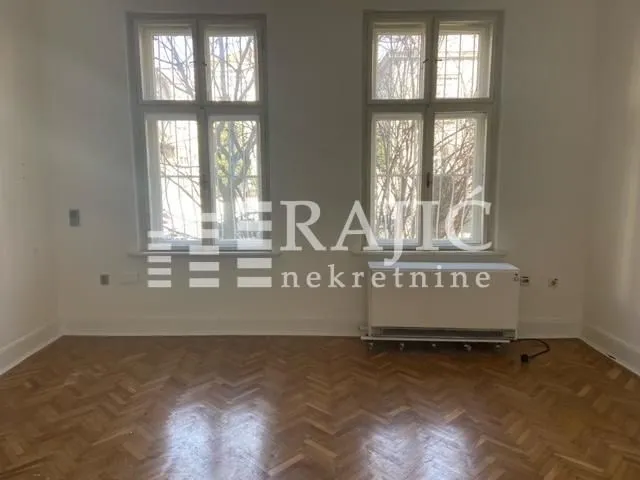 Empty room with parquet flooring and two windows.