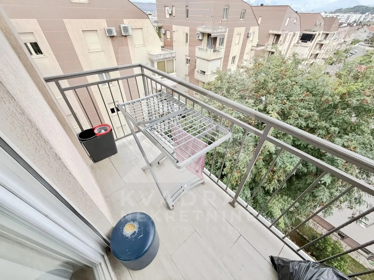 Manji balkon sa metalnom ogradom i pogledom na okolne zgrade i zelenilo.