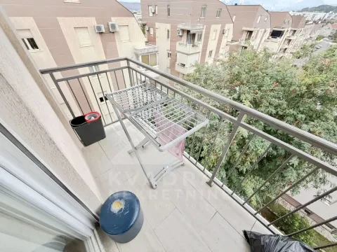 Manji balkon sa metalnom ogradom i pogledom na okolne zgrade i zelenilo. - image 10