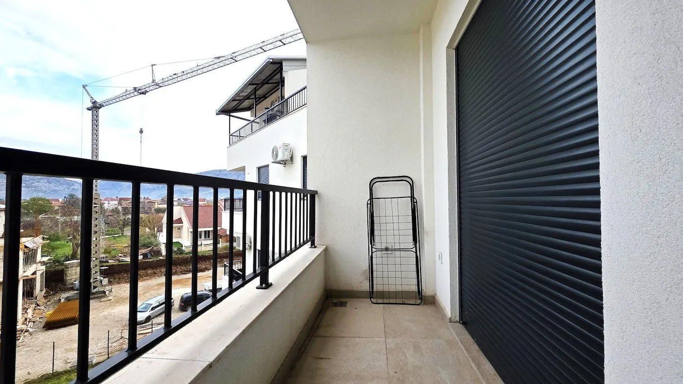Covered balcony with black railing and roller shutters on the windows.