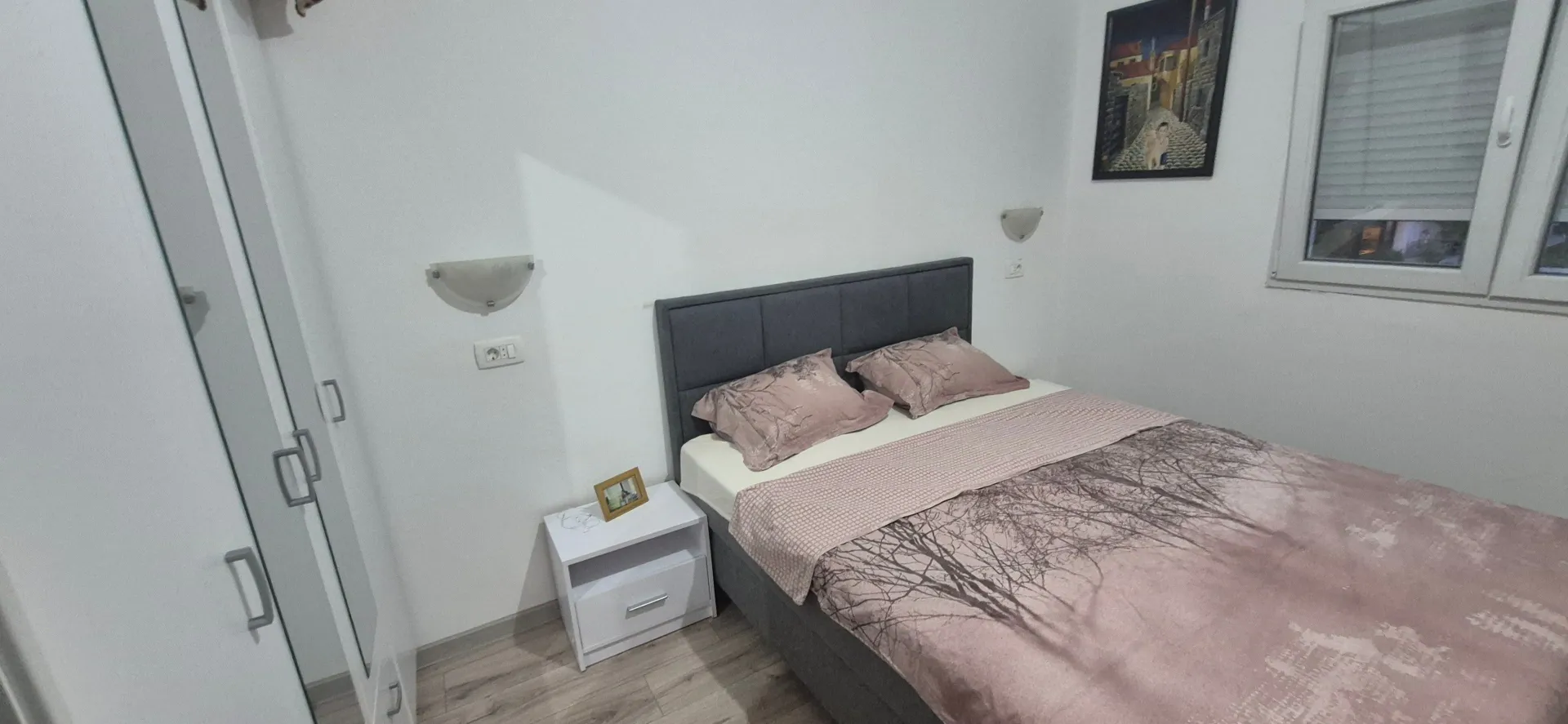 Namještena spavaća soba sa bračnim krevetom, bijelim garderoberom i noćnim stočićem.