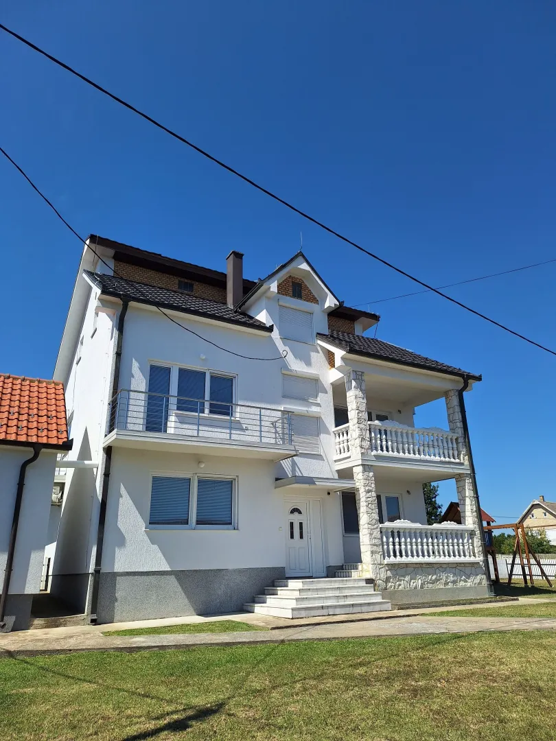 Eksterijer dvospratne kuće sa belom fasadom i terasama.