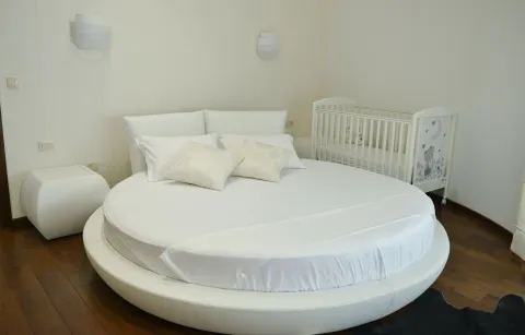 Spavaća soba sa velikim okruglim krevetom i krevetcem za bebe. - image 2
