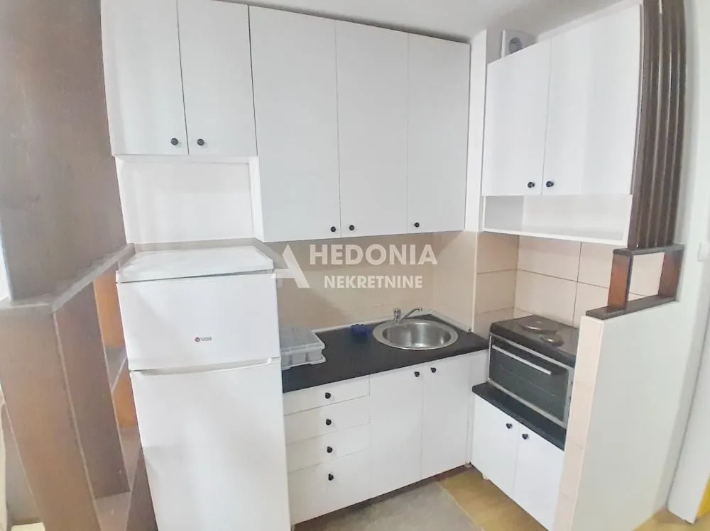 Manja kuhinja sa belim elementima, frižiderom i sudoperom.
