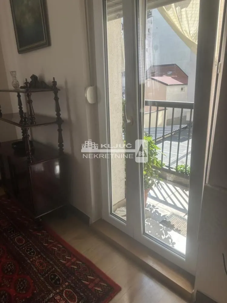 Pogled kroz balkonska vrata na terasu i okolne zgrade.