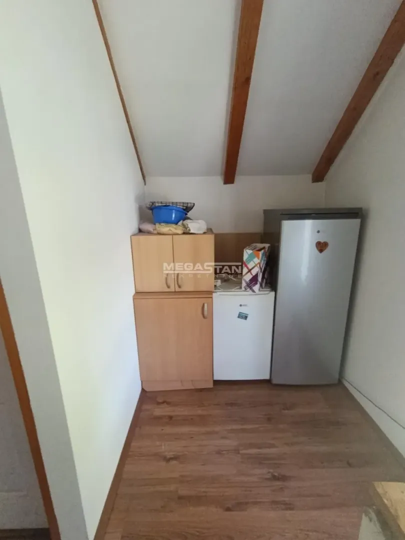 Small kitchen in the attic with wooden cabinets and a refrigerator.