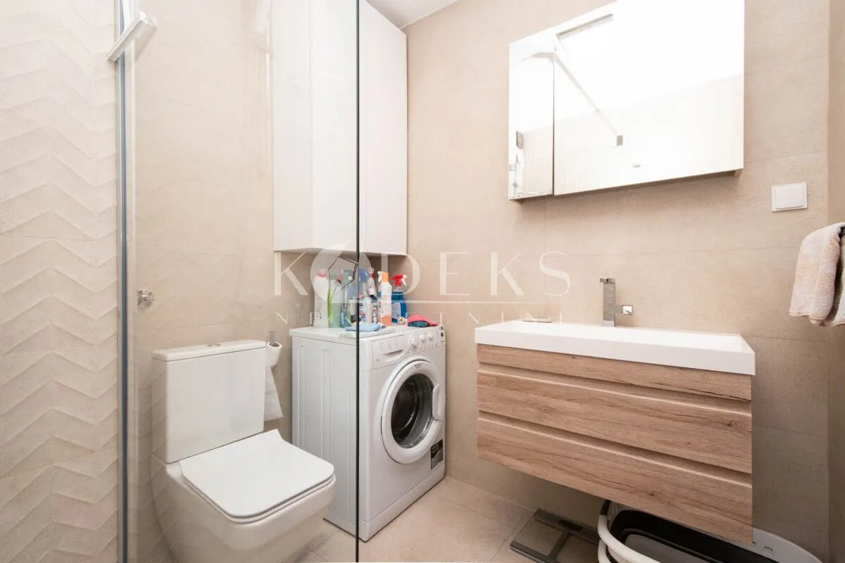 Modernly equipped bathroom with a shower cabin, washbasin, and washing machine.