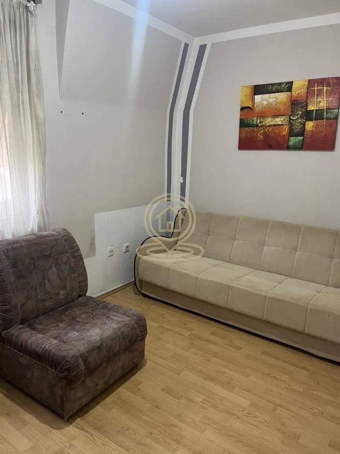 Dnevna soba sa kaučem, foteljom i umetničkom slikom na zidu.