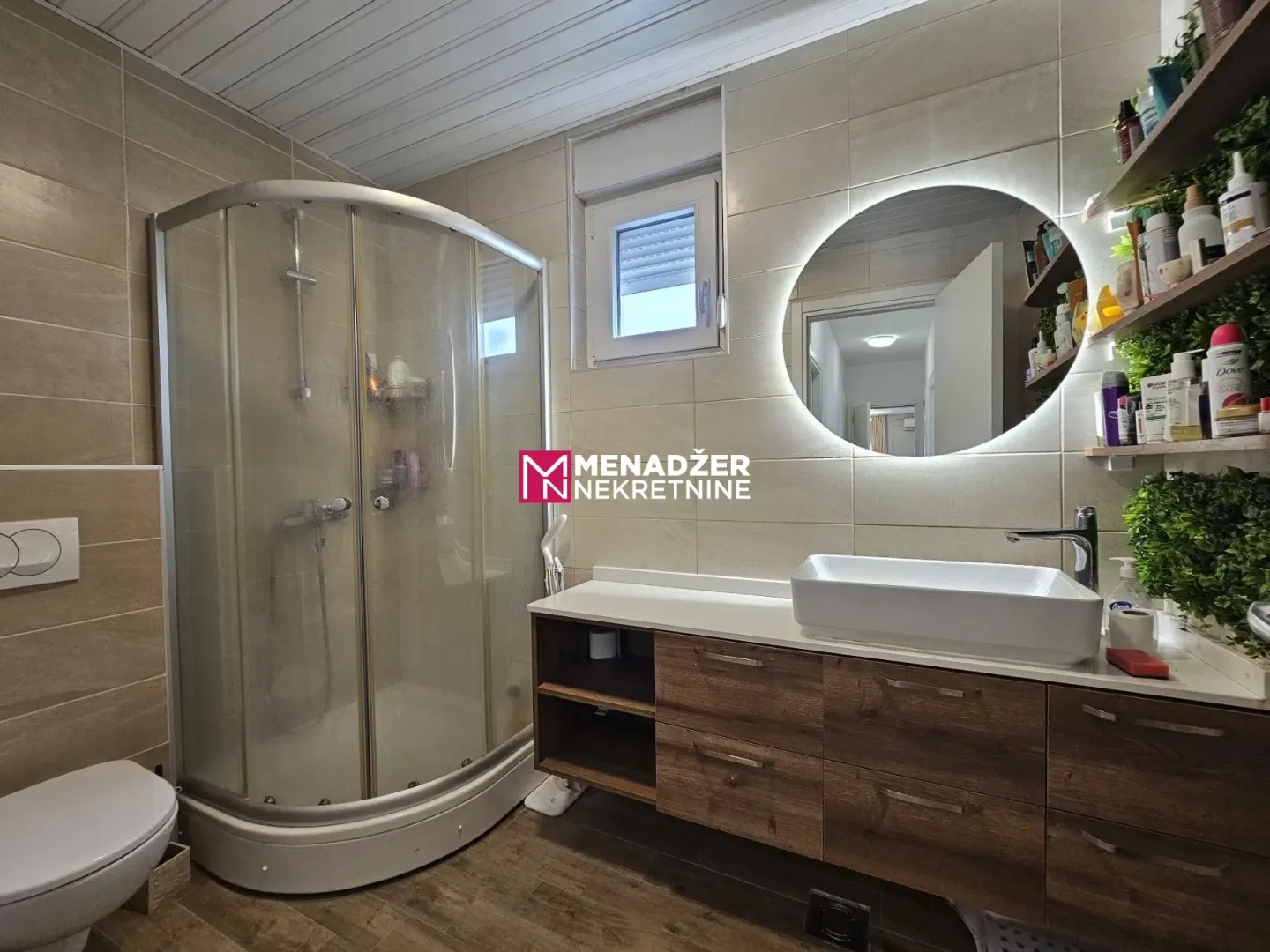 Modernly equipped bathroom with a shower cabin, washbasin, and backlit mirror.