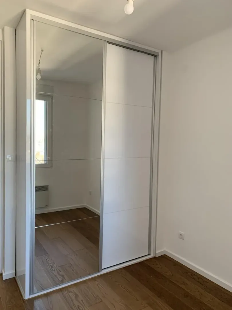 White built-in wardrobe with a mirrored sliding door in the room.