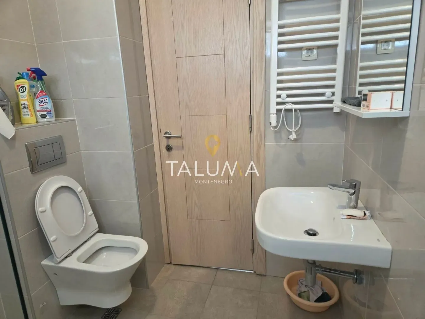 Small bathroom with a toilet, washbasin, and a light wood-toned door.