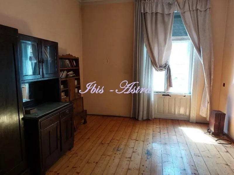 Spacious room with a wooden floor, dark cabinets, and a large window with curtains.