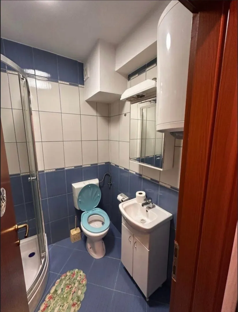 Manje kupatilo sa tuš kabinom, umivaonikom i plavo-bijelim pločicama.