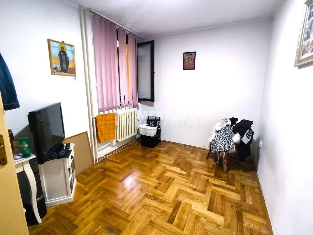 Manja soba sa parketom, prozorom i televizorom.
