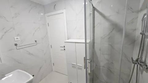 Moderne kupatilo obloženo keramičkim pločicama sa tuš kabinom i bijelim ormarićem. - image 3