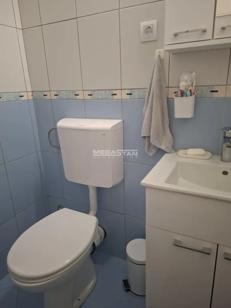 Manje kupatilo sa pločicama, wc šoljom i umivaonikom sa ormarićem.