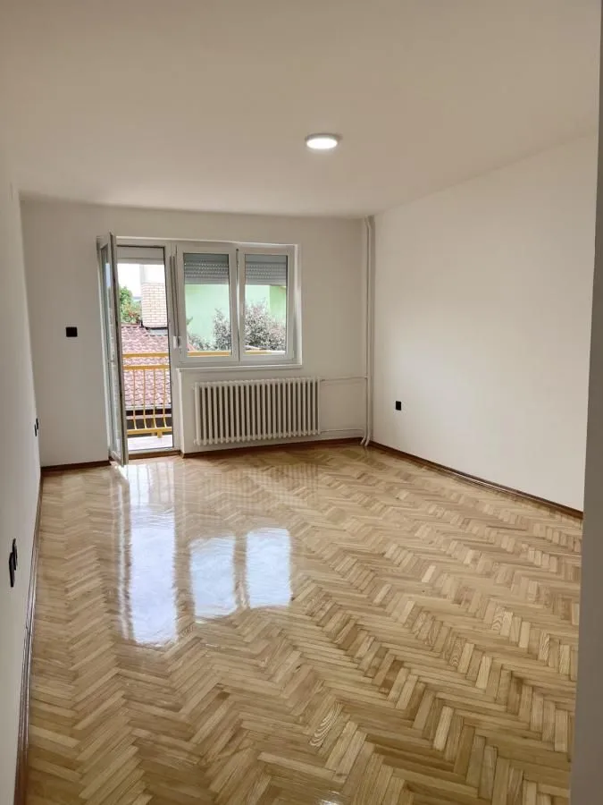 Prazna soba sa parketom i izlazom na balkon.