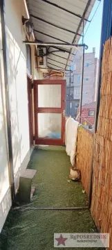 Uski natkriveni balkon sa veštačkom travom na podu i pogledom na okolne zgrade. - image 10