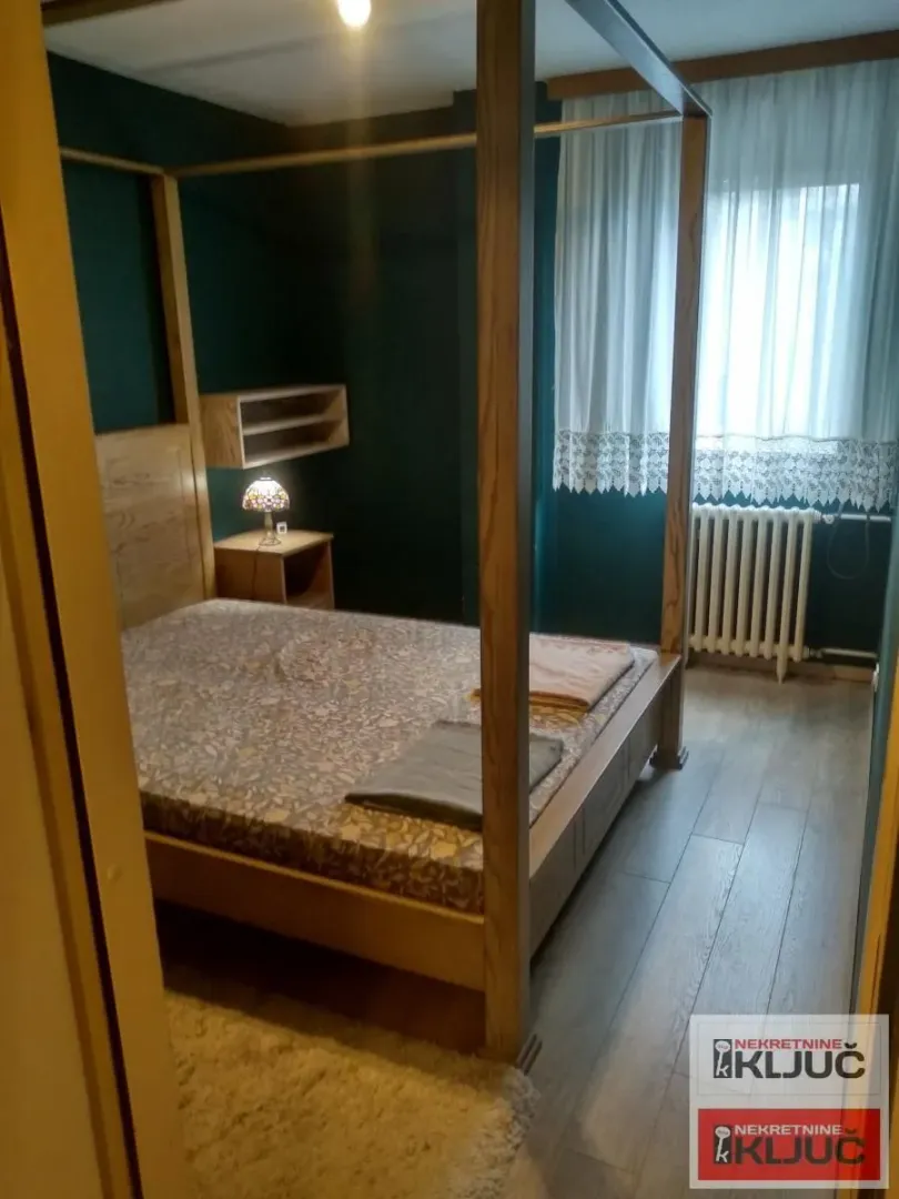 Spavaća soba sa velikim drvenim krevetom sa stubovima i tamnozelenim zidovima.