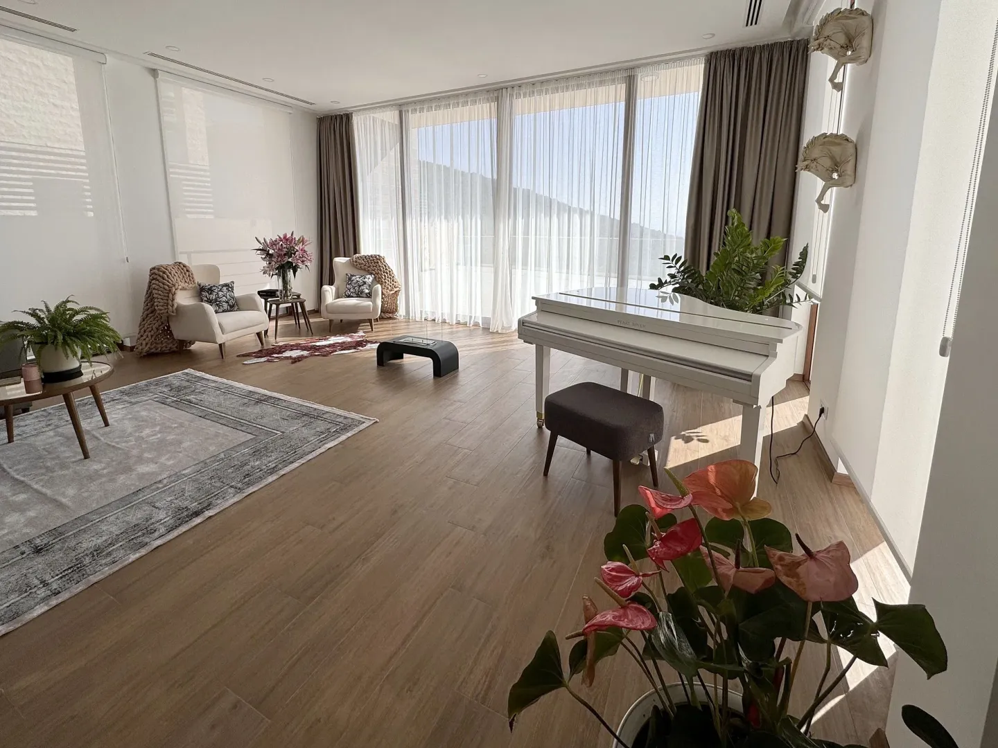 Spacious living room with a piano and large windows offering a view of the outside.