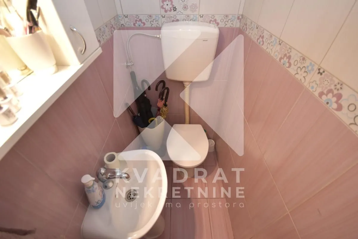 Manje kupatilo sa roze pločicama, wc šoljom, umivaonikom i dekorativnom bordurom.