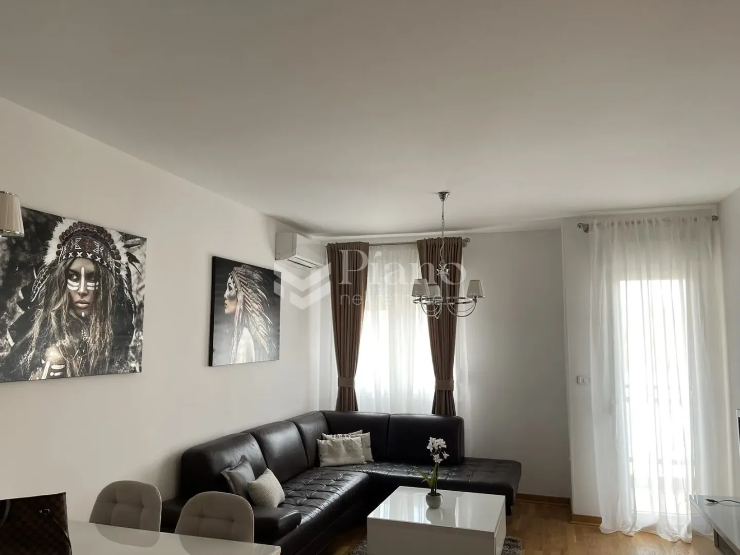 Dnevni boravak sa ugaonom garniturom, trpezarijskim stolom i umjetničkim slikama na zidu.