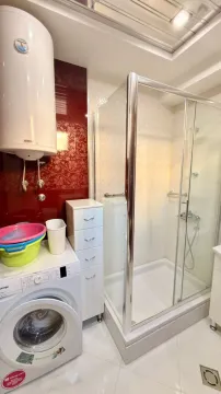 Bathroom equipped with a shower cabin, washing machine, and water heater. - image 9