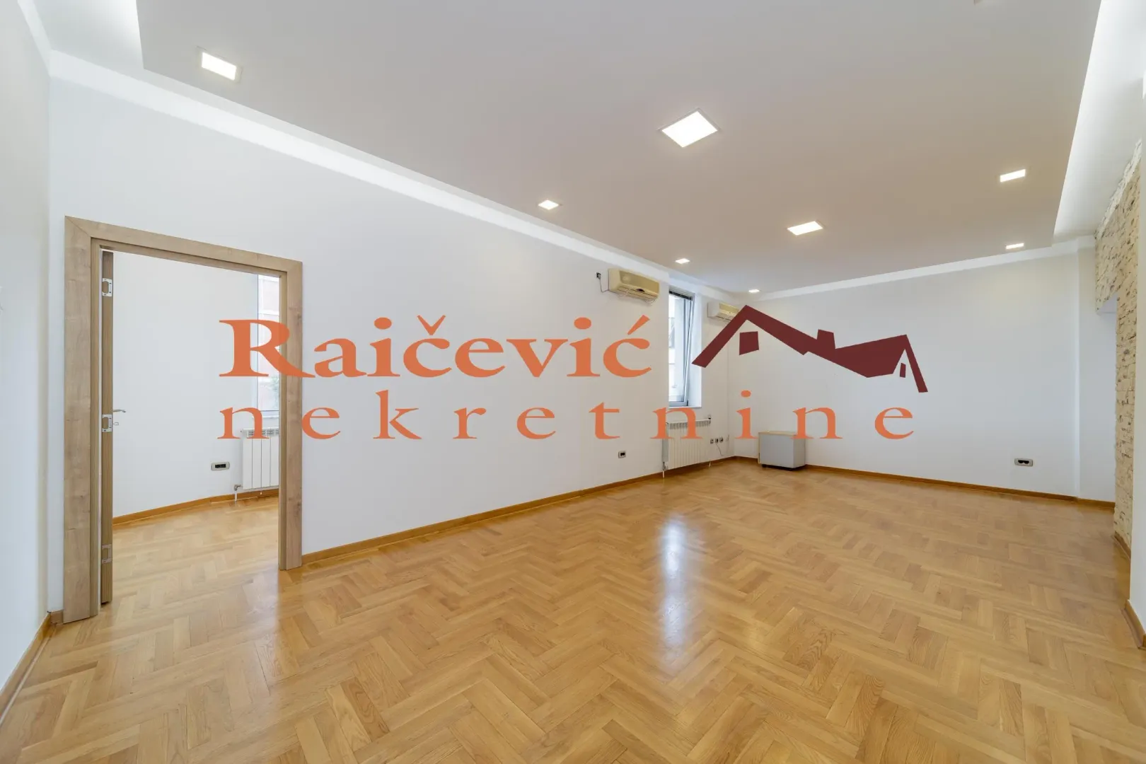 Empty living room with hardwood parquet flooring and recessed lighting.