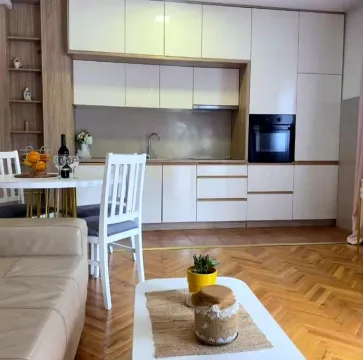 Moderna kuhinja sa bijelim elementima i trpezarijskim stolom, povezana sa dnevnim boravkom. - image 3