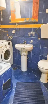 Kupatilo obloženo pločicama u plavoj boji sa umivaonikom, WC šoljom i veš mašinom. - image 5