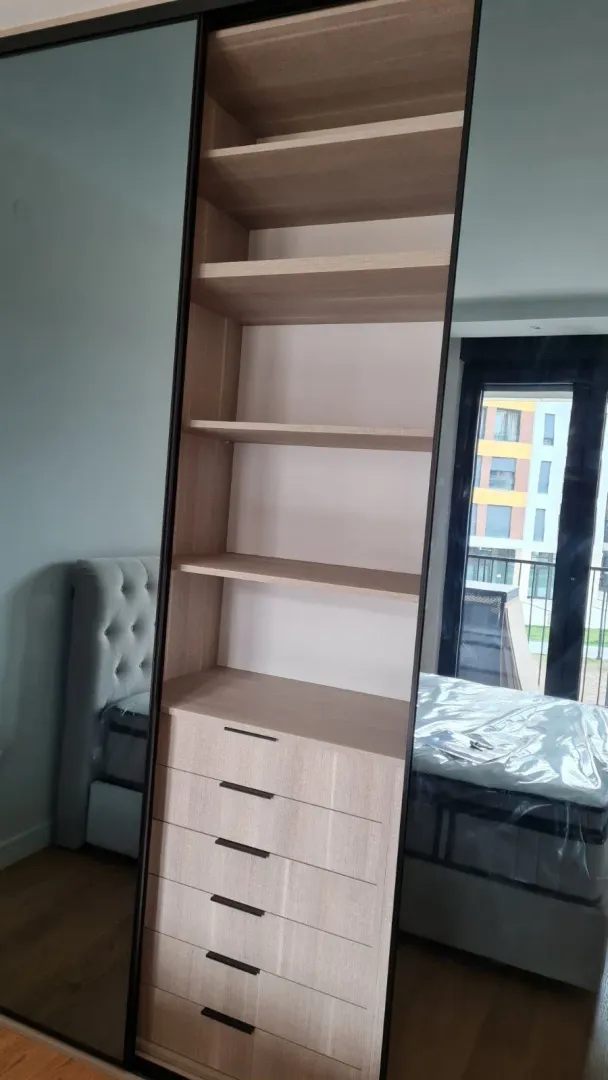 Built-in wardrobe with shelves and drawers in a bedroom.