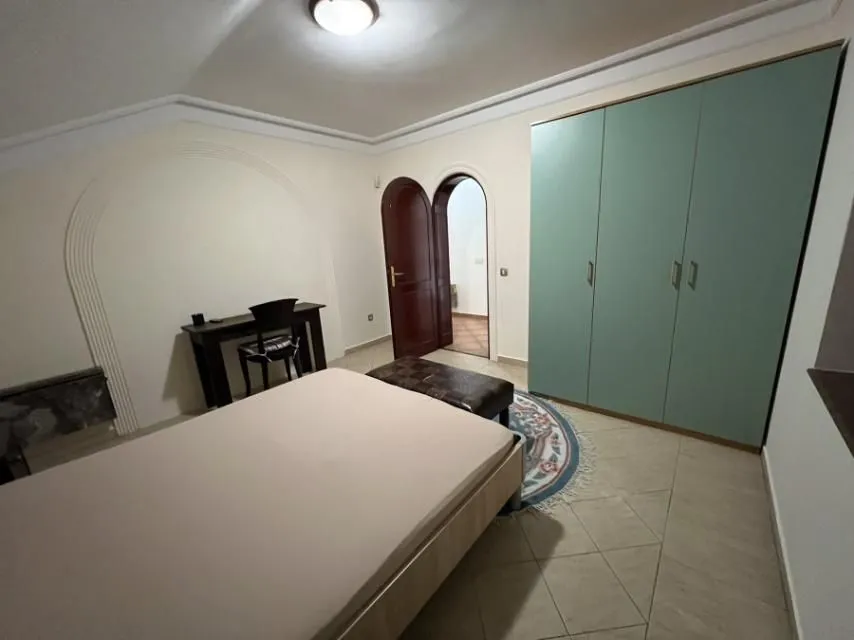 A simply furnished bedroom featuring a bed, wardrobe, and a small desk.