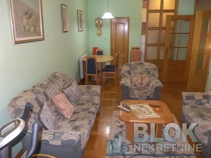 Living room with sofa, coffee table, and a dining area in the background.