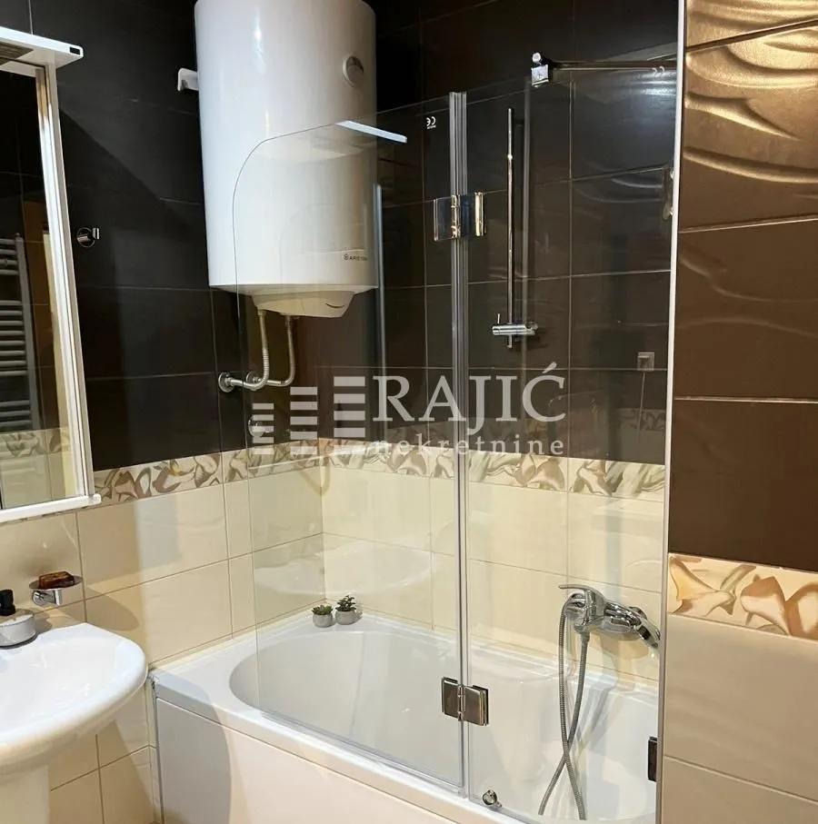 Small bathroom with a bathtub, shower screen, and water heater.