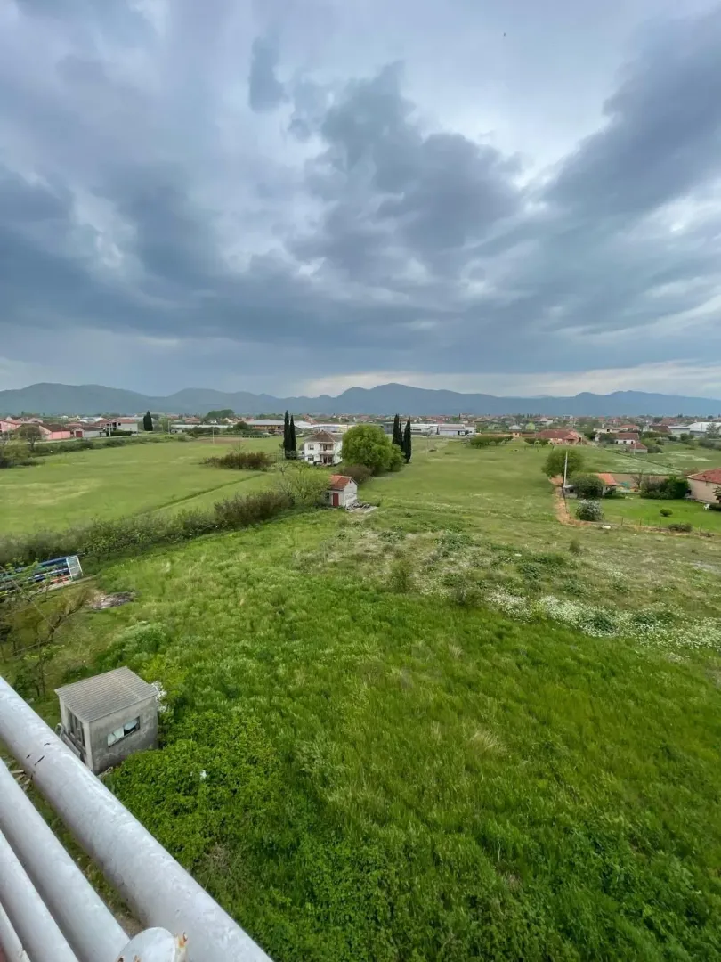 Pogled sa terase na prostrane zelene poljane pod oblačnim nebom.