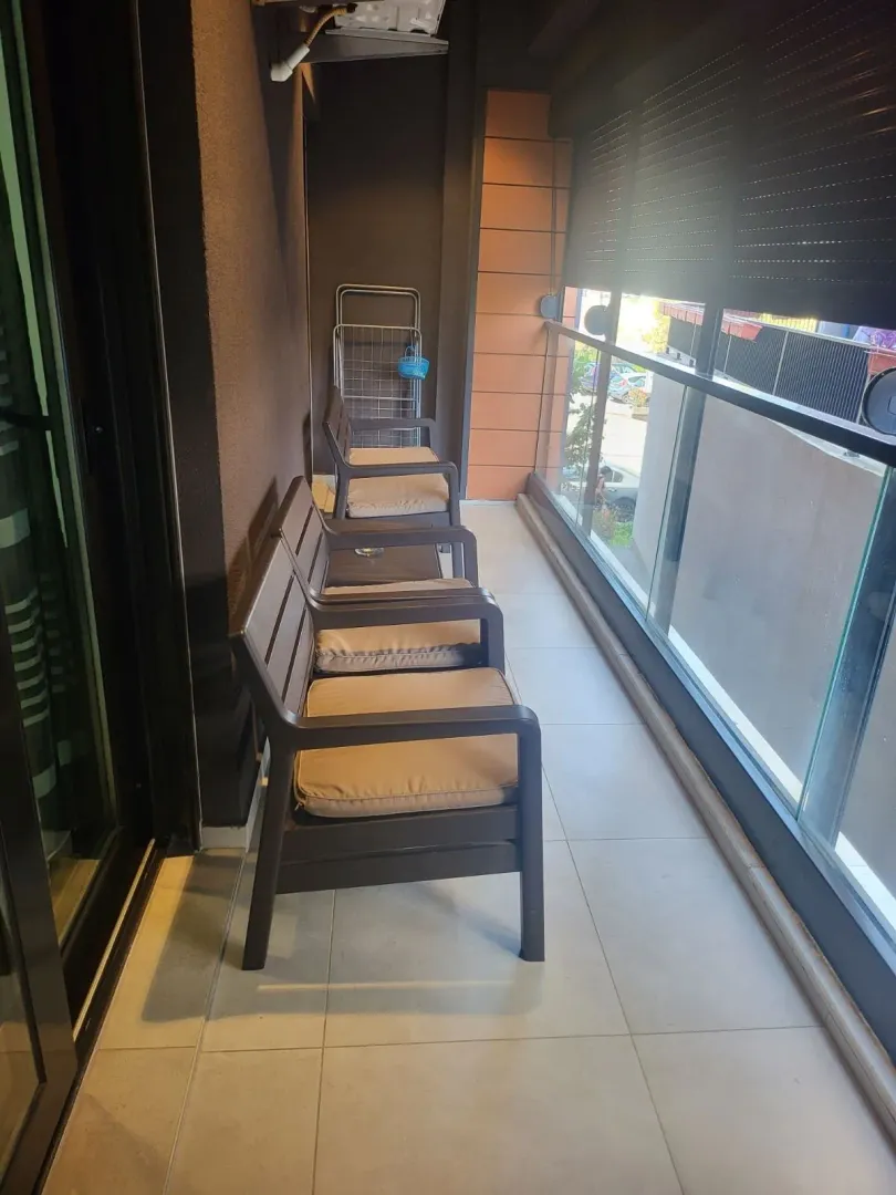 Narrow balcony with outdoor seating and a glass railing.