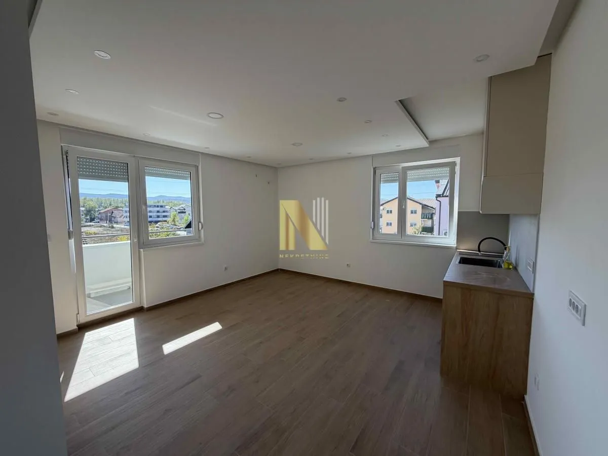 Spacious bright living room with laminate flooring, access to the terrace, and a small kitchenette area.