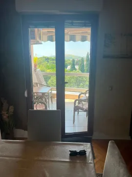 Pogled iz enterijera kroz balkonska vrata na terasu i zelenilo. - image 2