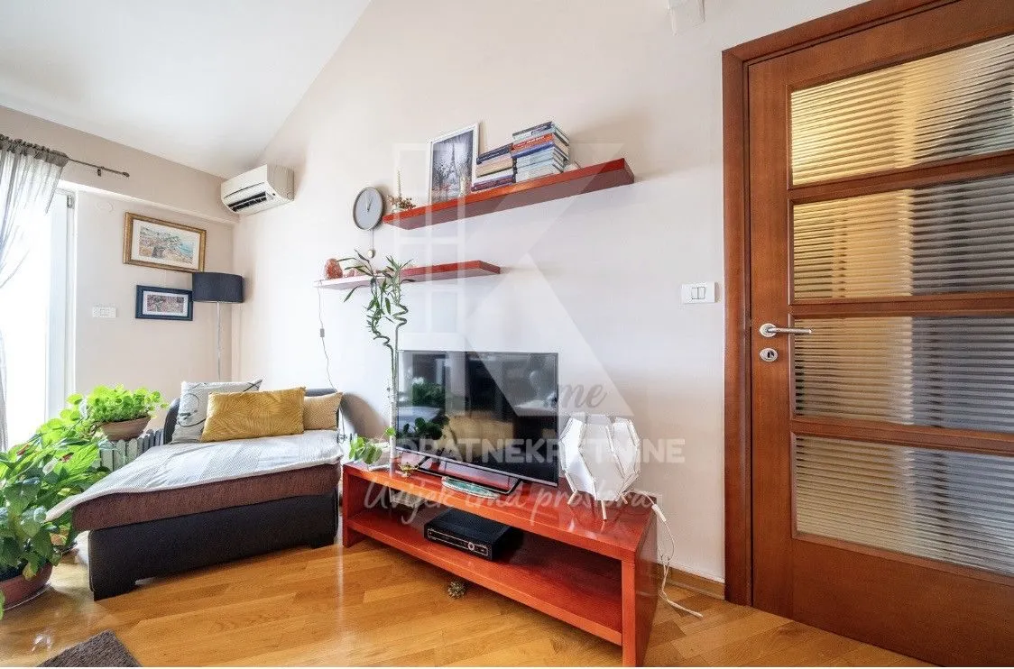 Living room with a sofa, TV stand, and wooden flooring.