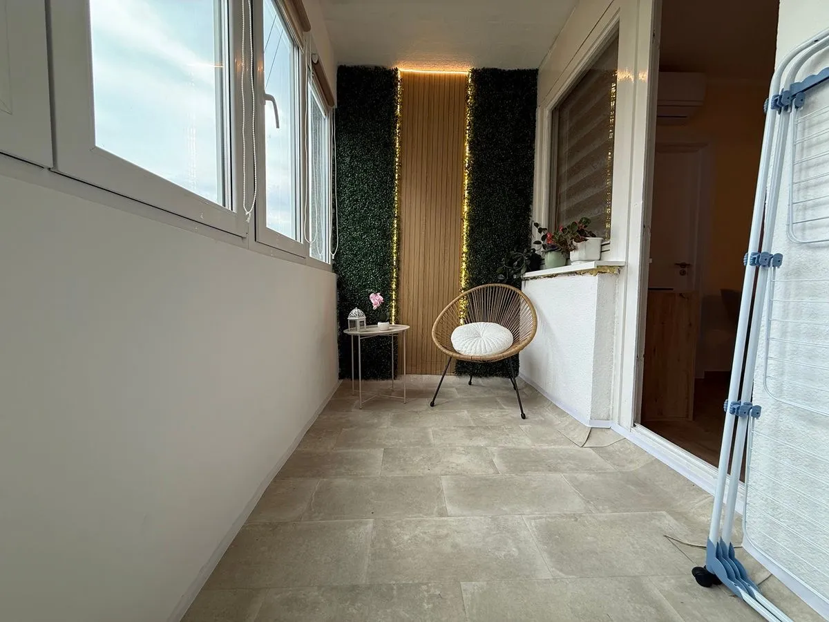 Zastakljeni balkon sa stolicom, malim stočićem i dekorativnim zidom.
