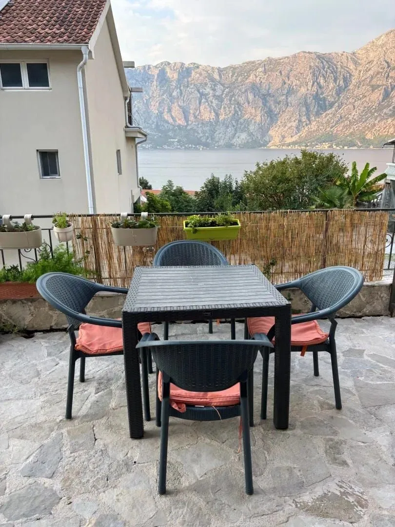 Namještena terasa sa stolom i stolicama i pogledom na more i planine.