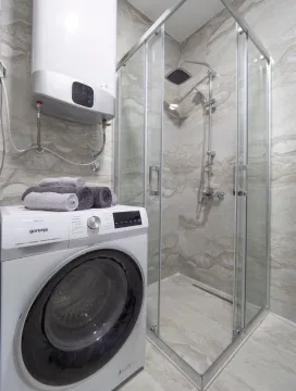 Bathroom with a shower cabin, washing machine, and water heater. - image 8