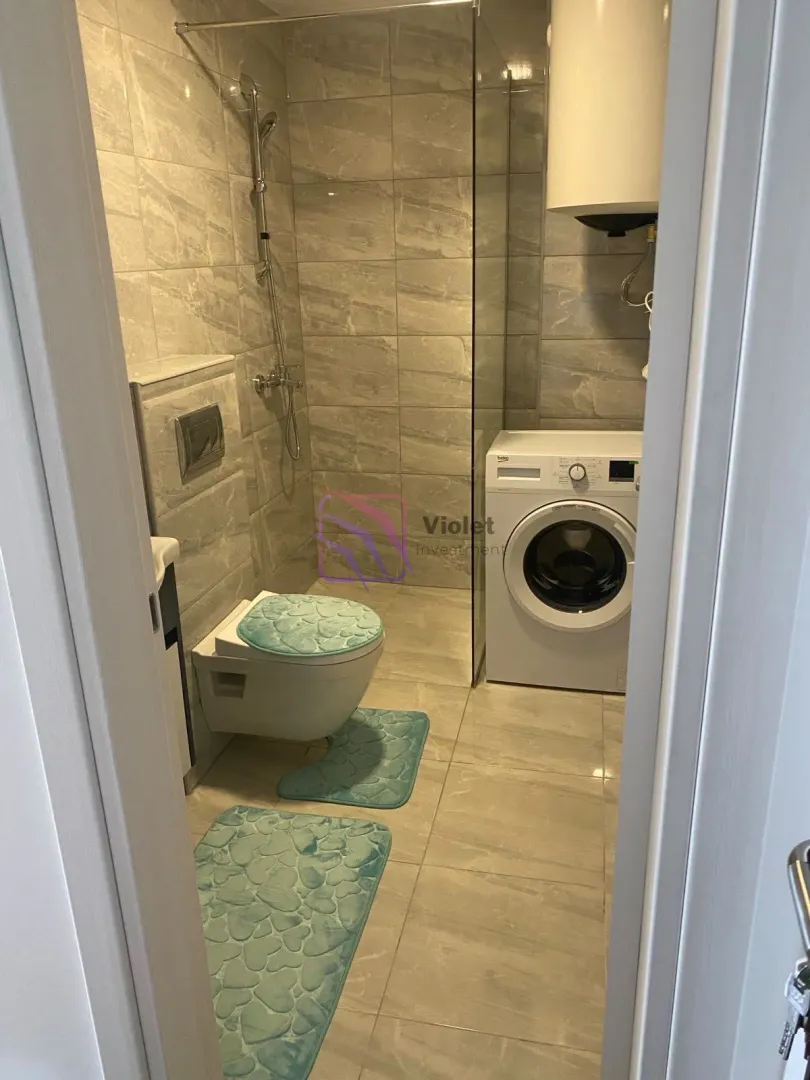 Moderne kupatilo sa tuš kabinom, wc šoljom i veš mašinom.